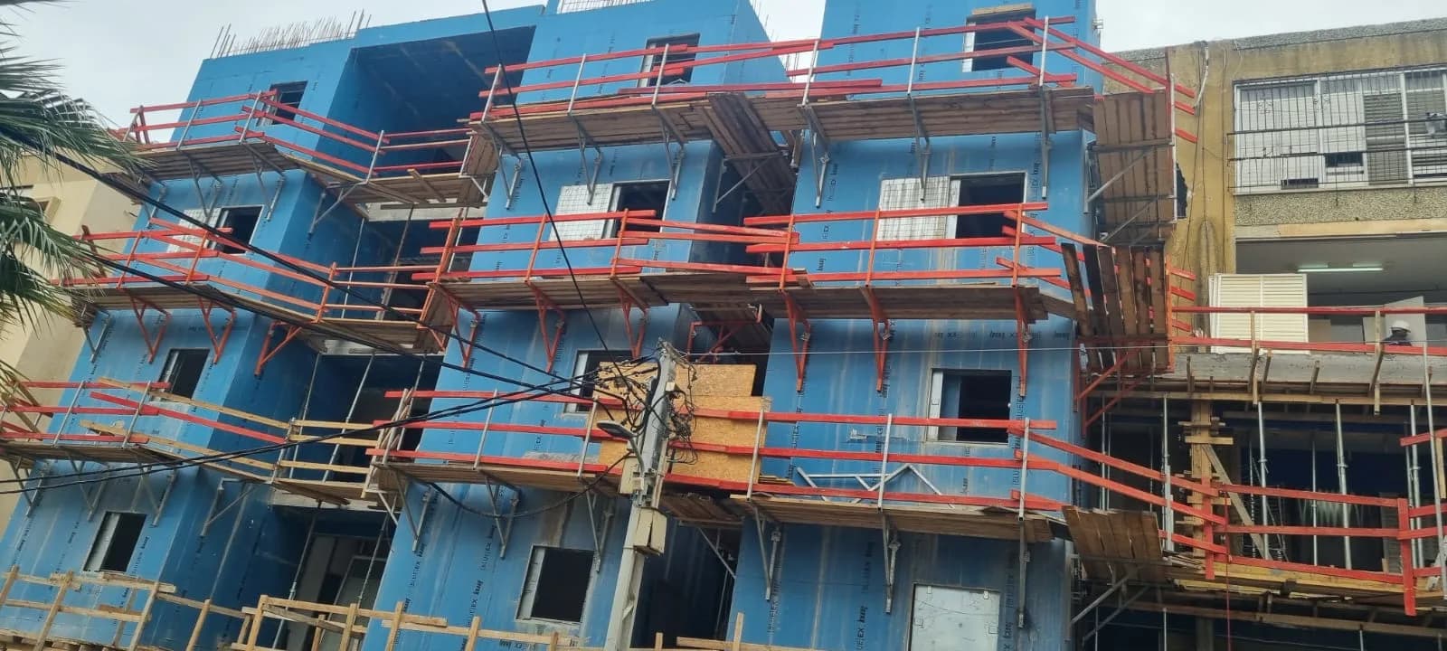 בניין מגורים בשלד עם קירות פרפב כחולים ופיגומים בשלב בנייה