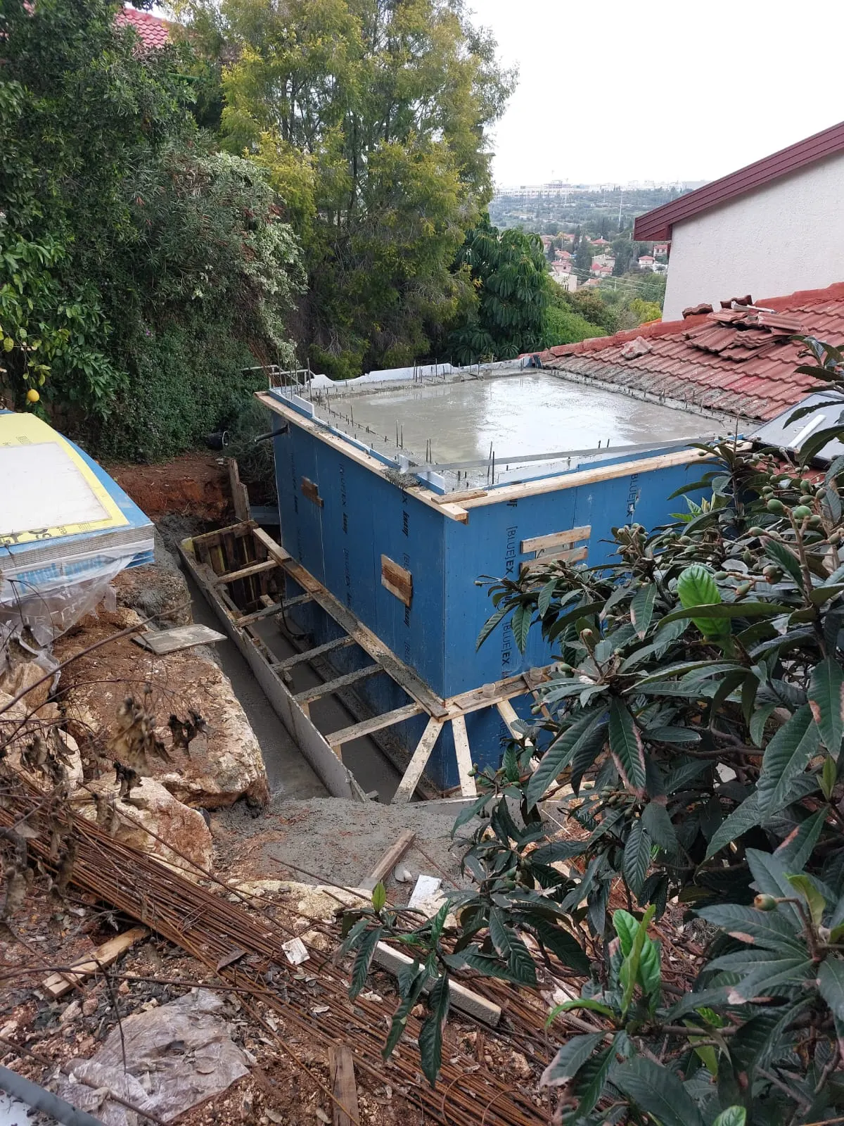 יציקת בטון על אלמנט iForm באתר, לצד בית פרטי עם גג רעפים